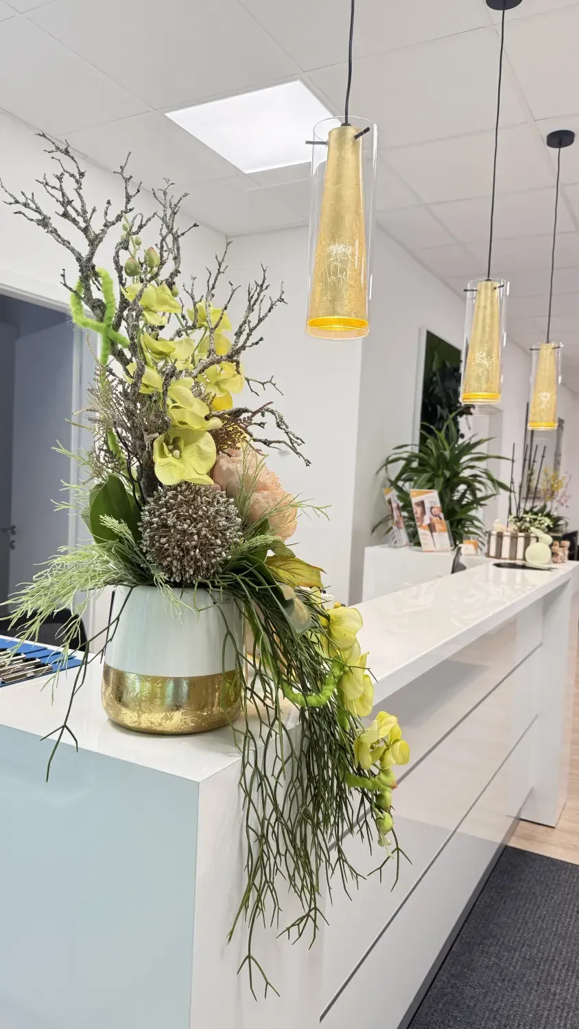 Empfangsbereich der Praxis: Blumenarrangement unter goldenen Pendelleuchten